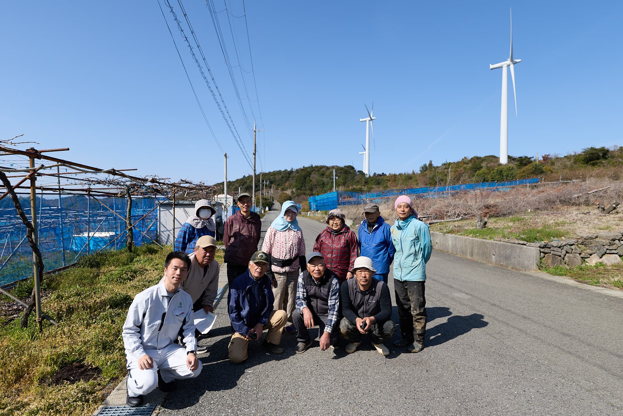 風力発電タービンを背景に農家さん10名と集合写真