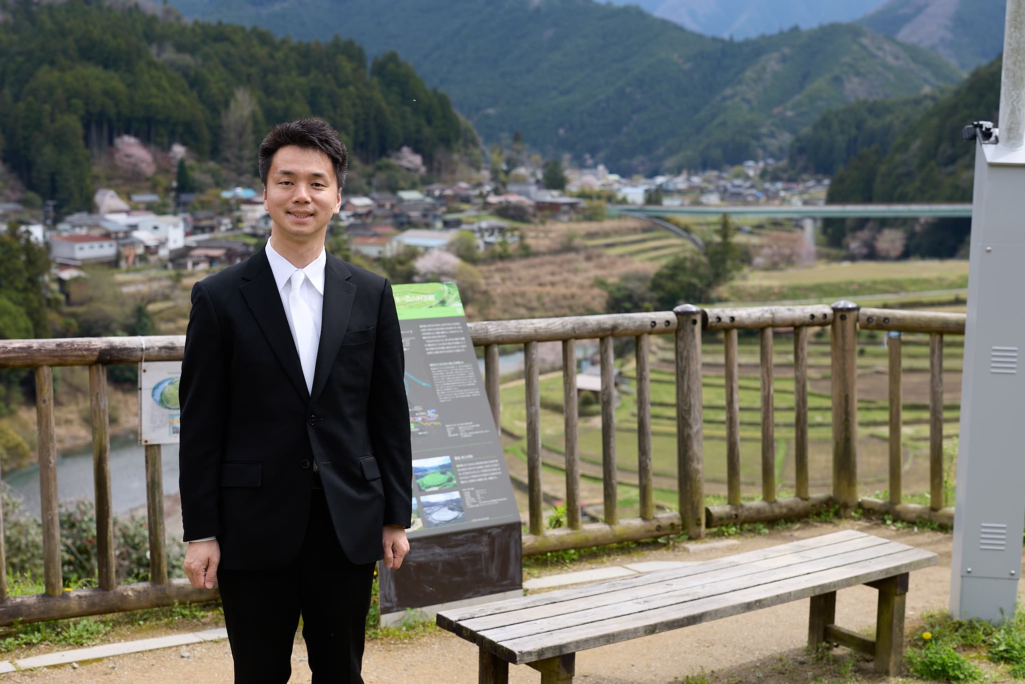 展望台で棚田と町並みを背に立つ、ベンチと案内板
